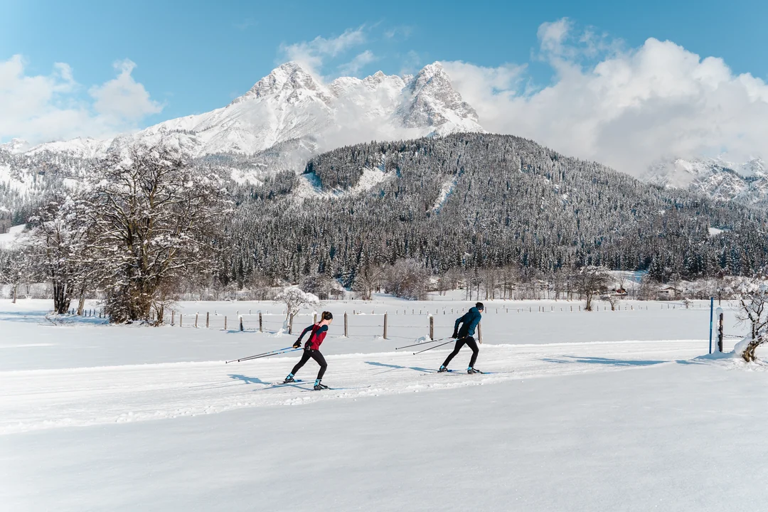 Zwei Langläufer auf einer Loipe vor winterlicher Bergkulisse