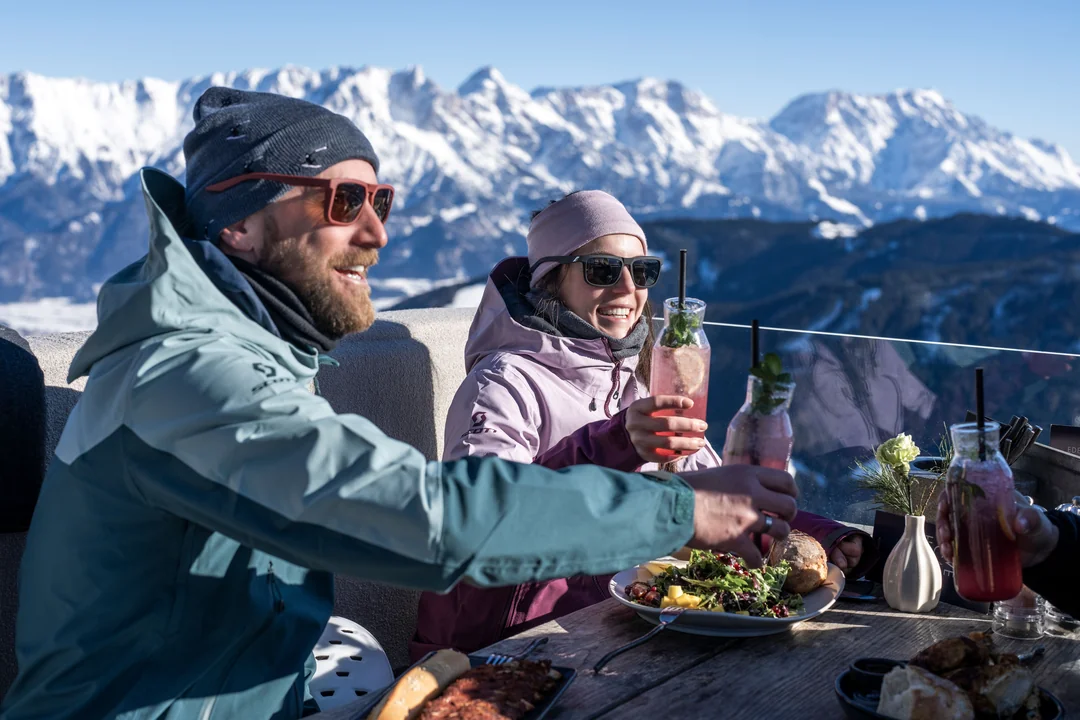 Pareja disfrutando de cócteles en la terraza soleada con vistas a los Steinberge en invierno
