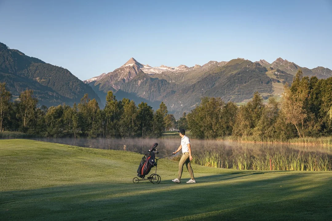 Golfeur avec un chariot sur le fairway du Golfclub Zell am See-Kaprun devant le Kitzsteinhorn dans la lumière du matin