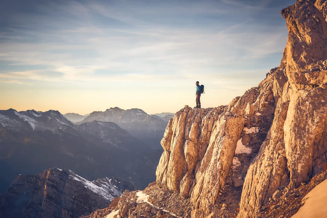 Climber on rock ledge with alpine panorama at sunset