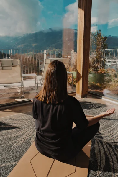 Frau meditiert im Schneidersitz mit Blick auf die Dachterrasse durch Glasfront