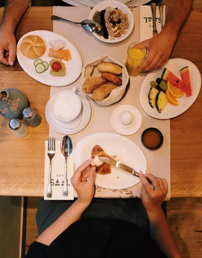 Frühstückstisch von oben mit verschiedenen Tellern und Händen beim Essen