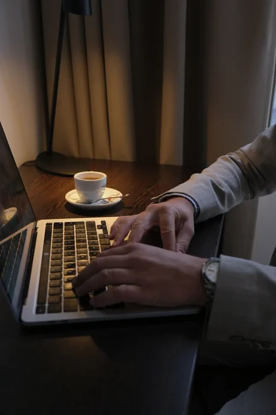 Hände tippen auf Laptop-Tastatur neben Espressotasse am Schreibtisch