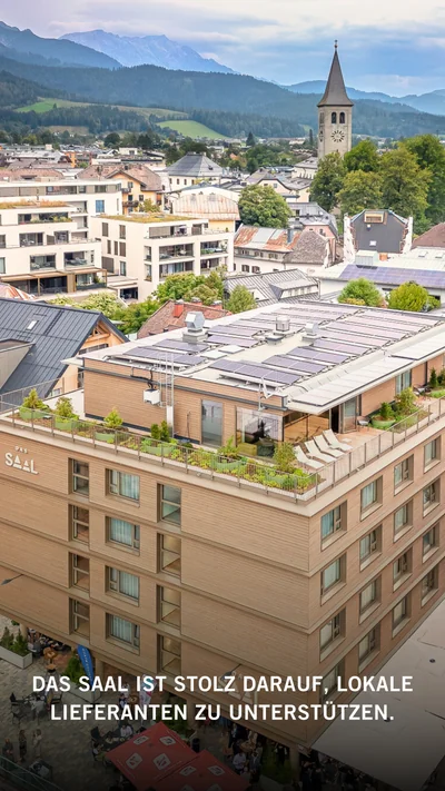 Luftaufnahme Hotel DAS SAAL mit begrünten Dachterrassen, Solaranlagen und Kirchturm