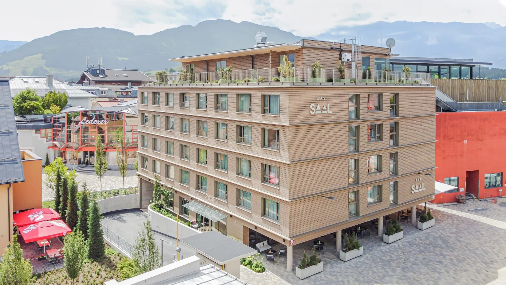 DAS SAAL Hotel Außenansicht mit Holzfassade, Dachterrasse und angrenzendem Congress Saalfelden, Bergpanorama im Hintergrund