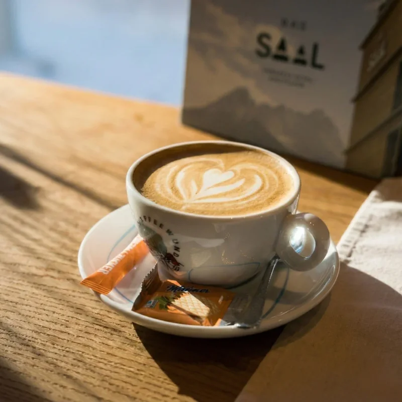 木桌上的卡布奇诺配拉花心形图案，带DAS SAAL品牌标识