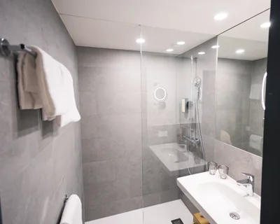 Komplettansicht des modernen Badezimmers mit ebenerdiger Dusche, Kosmetikspiegel und Handtüchern