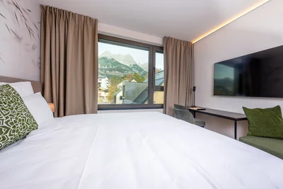 Bett-Perspektive mit grünem Akzentkissen, Bergblick und TV-Bereich