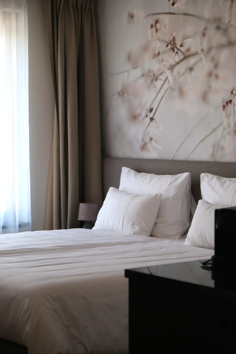 Gemütliches Doppelzimmer Classic mit zartem Blütenmotiv-Wandbild, weißer Bettwäsche und beigen Vorhängen