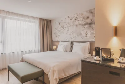 Helles Doppelzimmer Classic mit zartem Blütenwandbild, grüner Sitzbank und Minibar-Station