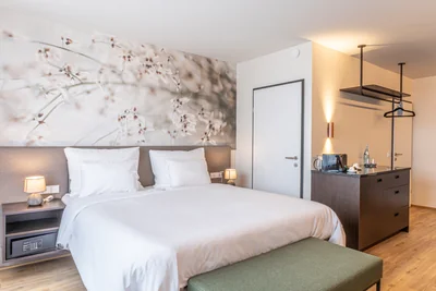 Einladendes Doppelzimmer Classic mit großflächigem Blütenwandbild, grüner Sitzbank und Minibar