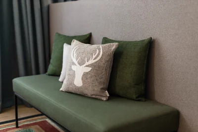 Grüne Sitzbank mit alpinem Hirschkopf-Kissen und dunkelgrünen Dekokissen