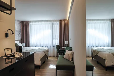 Geräumiges Doppelzimmer mit zwei Einzelbetten, grüner Sitzecke und indirekter LED-Deckenbeleuchtung