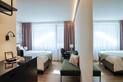 Doppelzimmer mit zwei Einzelbetten, grüner Mittelbank und indirekter Deckenbeleuchtung