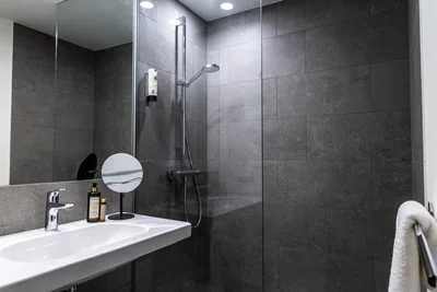 Elegantes Badezimmer mit anthrazitfarbenen Fliesen, begehbarer Glasdusche und Damana Pflegeprodukten