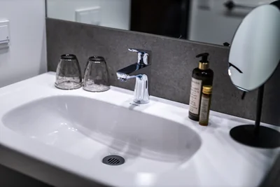 Waschtisch-Detail mit Damana Pflegeprodukten, Trinkgläsern und Kosmetikspiegel