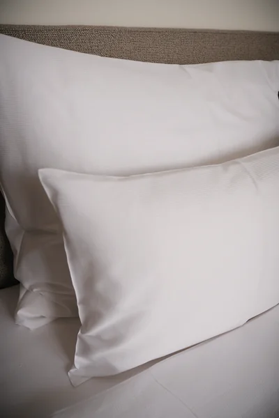 Luxuriöse weiße Kissen auf hochwertigem Hotelbett mit Stoffkopfteil