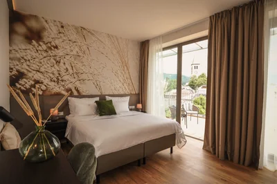 Executive Suite mit Doppelbett, eleganter Gräser-Wandtapete und Balkon mit Blick auf den Saalfeldener Kirchturm