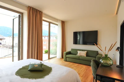 Geräumige Executive Suite mit Doppelbett, grünem Sofa und großer Balkontür mit Bergblick