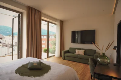 Executive Suite mit Doppelbett, olivgrünem Sofa, Flatscreen-TV und Balkontür mit Stadtblick