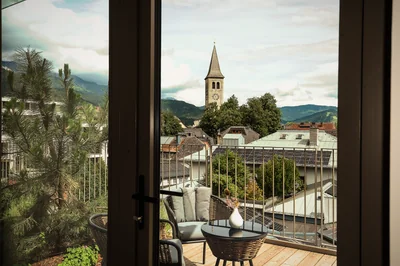 Terrasse der Executive Suite mit Rattanmöbeln und Blick auf Saalfeldener Kirchturm und Berge