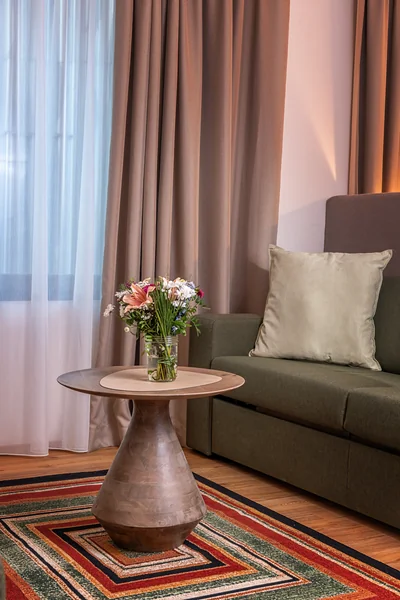 Eleganter Holz-Beistelltisch mit frischem Blumenstrauß auf buntem geometrischem Teppich