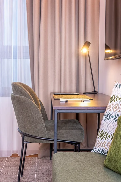 Stilvoller Arbeitsbereich mit dunklem Holzschreibtisch, grünem Designerstuhl und eleganter Schreibtischlampe