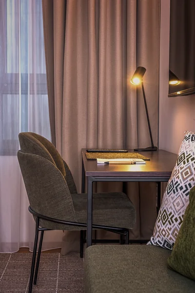 Atmosphärischer Arbeitsbereich mit Designer-Schreibtischlampe und grünem Polsterstuhl