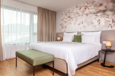 Einladendes Doppelbett mit zartem Blütenwandbild, grünem Kissen und natürlichem Lichteinfall