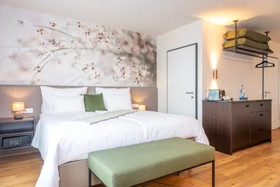 Junior Suite mit großflächigem Blütenwandbild, grünem Akzentkissen und Minibar-Regal