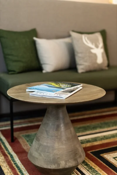 Gemütliche Sitzecke mit grünem Sofa, Hirschkopf-Kissen und Reisemagazinen auf Beistelltisch