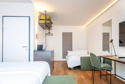 Blick auf Tagesbett mit Handtüchern, offene Garderobe und Minibar-Bereich