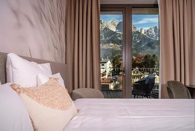 Elegantes Schlafzimmer mit Feder-Tapete, orangem Akzentkissen und Steinberge-Blick