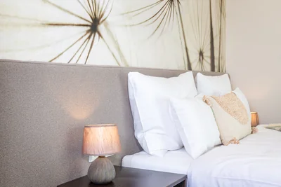 Detail Kopfteil mit Pusteblumen-Tapete, Nachttischlampe und Quasten-Kissen