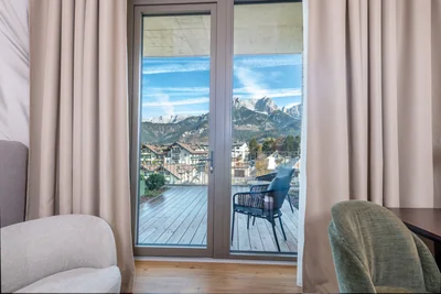 Balkonblick auf Steinberge-Panorama durch Glastür mit Rattanstuhl