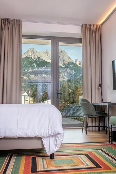 Schlafzimmer mit Streifenteppich und Steinberge-Panorama durch bodentiefes Fenster