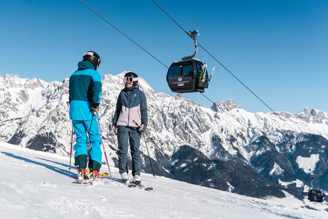 Skifahrer-Paar neben Gondelbahn mit Blick auf die verschneiten Steinberge